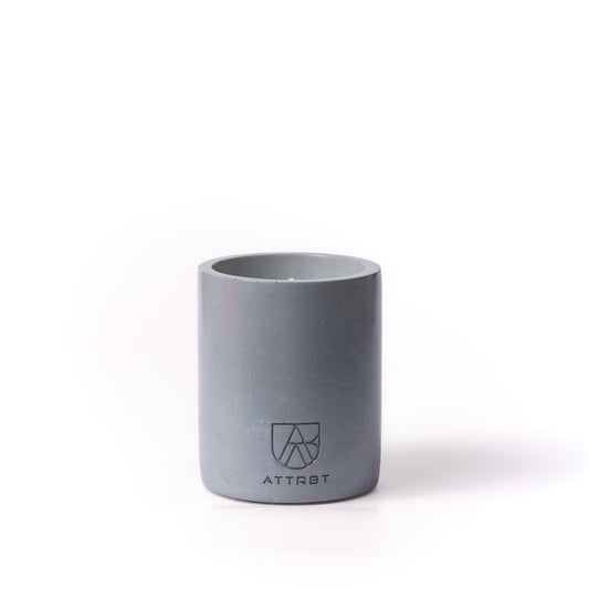 A minimalist one-wick candle in a dmatte dark gray color cylindrical concrete container, featuring the 'ATTRBT' brand logo on the front, set against a clean white background.
mineral. concrete candle